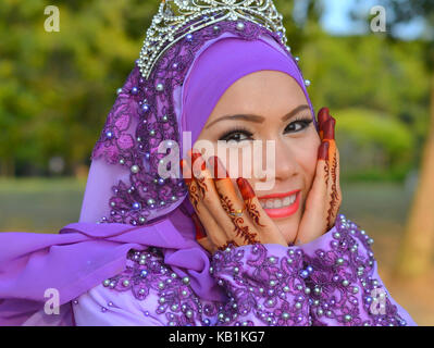 Beautiful traditional Muslim Malay bride with elaborate makeup and bridal henna on both her hands, wearing a blue bridal hijab and blue wedding dress Stock Photo