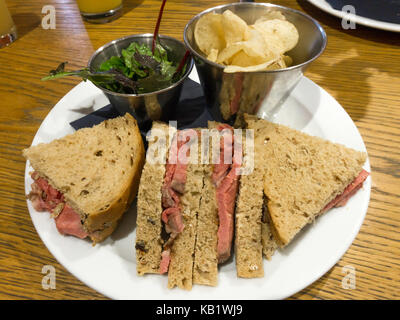 Lunchtime snack rare roast beef and horseradish mayonaisse sandwich in granary bread with rocket salad and potato crisps Stock Photo