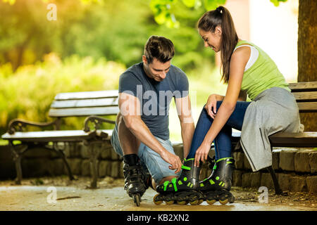 Young man helping his girlfriends to put rollerblades Stock Photo