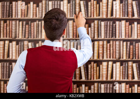 Male student take a book from the shelf in the library Stock Photo