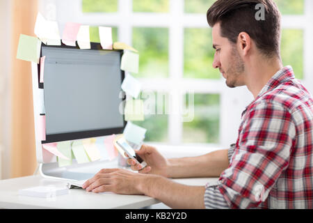 overworked man typing on computer with stickers on monitor Stock Photo