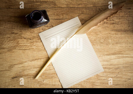 Empty letter paper with goose quill and inkpot on wooden table, top view Stock Photo