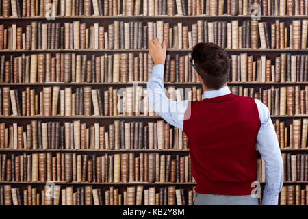 Young man in library take book from shelf Stock Photo