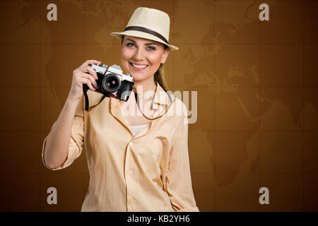 smiling female tourist holding photo camera with map world in background Stock Photo