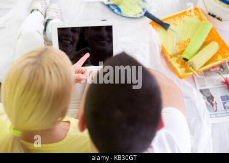 Couple taking break of painting house, they looking at tablet with their smile at reflection Stock Photo