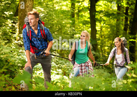 Three friends hiking through the forest, one male, two female, with backpacks Stock Photo