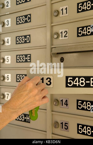 Caucasian Senior Female (age 60-70) opening  apartment complex mailbox with key, USA Stock Photo