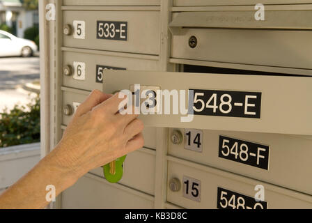 Caucasian Senior Female (age 60-70) opening  apartment complex mailbox with key, USA Stock Photo