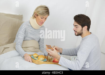 son assisting ill mother lying in bed Stock Photo