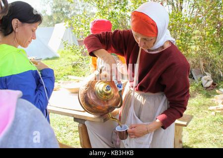 The International Military and Historical Festival 'Kulikovo Field': a woman in traditional clothes pours sbiten from a copper kettle. Stock Photo