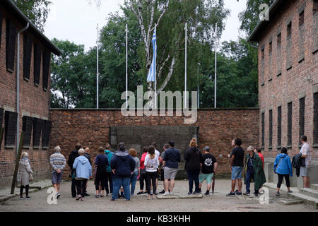 Tourists looking at a wall used for firing squad executions at the Auschwitz WWII Nazi concentration camp, Poland Stock Photo