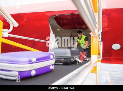 Mature male worker placing bags on conveyor to unload airplane Stock Photo