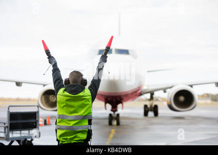 Rear view of ground crew signaling to airplane on wet runway Stock Photo