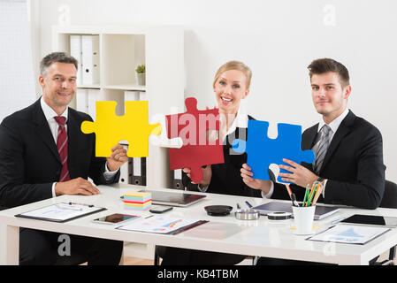 Team Of Happy Businesspeople Holding Multi-colored Jigsaw Puzzle In Office Stock Photo