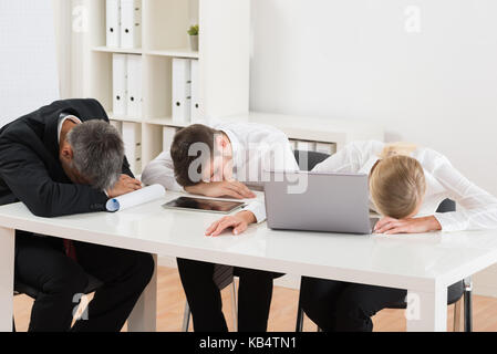 Group Of Businesspeople Sleeping At Desk In Office Stock Photo