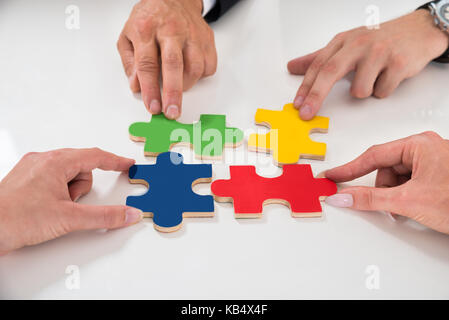 Close-up Of People Assembling Colorful Puzzle Pieces At Desk Stock Photo