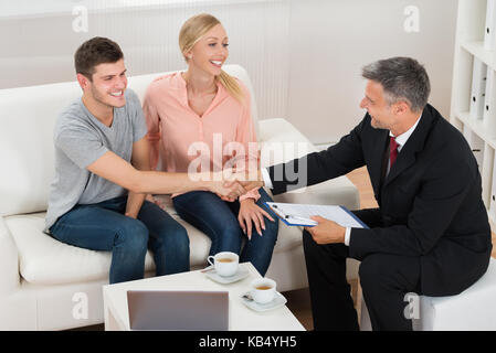 Mature Male Consultant Shaking Hands To Young Happy Man With Wife Stock Photo
