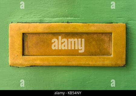 A well used unpolished brass letterbox on a roughly painted green front door in the UK. Stock Photo