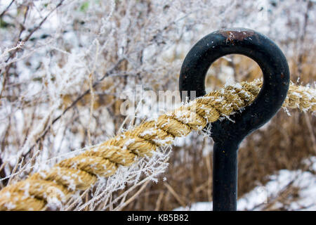 Thick rope covered in snow passing through an iron round hook Stock Photo