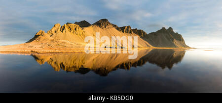 Panoramic view of mountains of Vestrahorn and perfect reflection in shallow water, soon after sunrise, Stokksnes, South Iceland Stock Photo