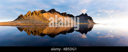 Panoramic view of mountains of Vestrahorn and perfect reflection in shallow water, soon after sunrise, Stokksnes, South Iceland Stock Photo