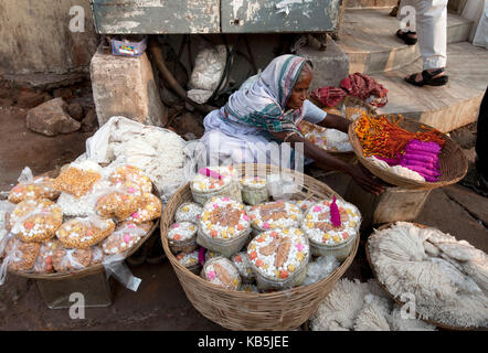 Woman in white sari, selling puja offerings in the street near the Hindu Jagannath temple of Vishnu, Puri, Odisha, India Stock Photo