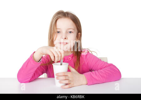 Cute little girl in red shirt drinking tea while sitting at table isolated on white background Stock Photo