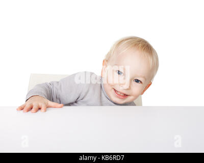 Cute little smiling boy sitting at table isolated on white background Stock Photo