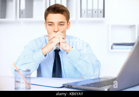 Portrait of young pensive businessman at his workplace in bright office Stock Photo