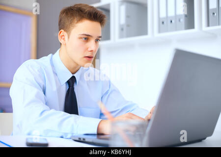 young serious businessman working on laptop in bright office