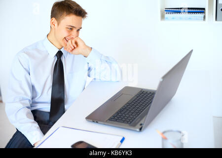Portrait of young laughing businessman looking at the laptop screen at his workplace in bright office Stock Photo