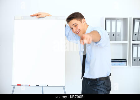 Young laughing businessman with a flip chart pointing to the camera on presentation Stock Photo