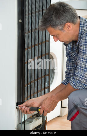 Cropped image of serviceman working on fridge with screwdriver at home Stock Photo
