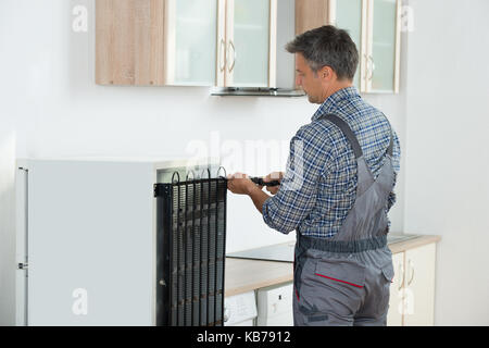 Cropped image of serviceman working on fridge with screwdriver at home Stock Photo