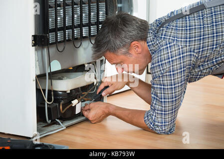 Cropped image of serviceman working on fridge with screwdriver at home Stock Photo