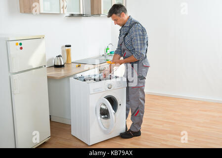 Full length of technician checking washing machine with digital multimeter in kitchen Stock Photo