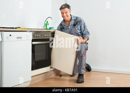 Full length of mature handyman fixing sink door in kitchen Stock Photo