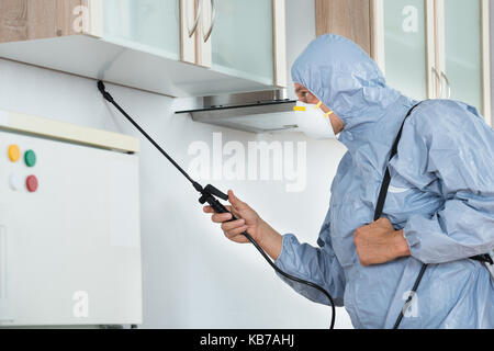 Side view of exterminator in workwear spraying pesticide in kitchen. Pest control Stock Photo