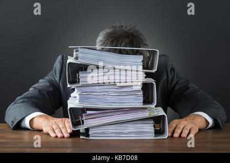 Frustrated businessman with lot of files on desk against gray background Stock Photo