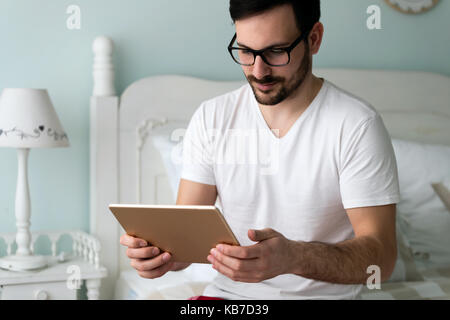 Young handsome man using digital tablet on bed Stock Photo