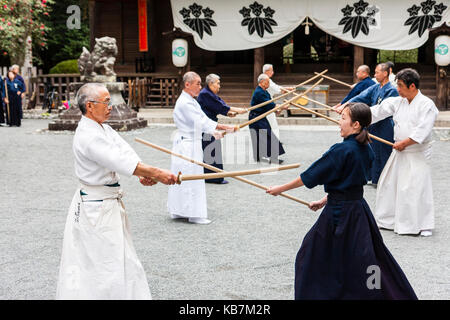 Japan, Osaka, Tada. Master samurai swordsman dressed in white fighting with woman in black, using bokken, or bokuto, wooden swords in shrine grounds. Stock Photo