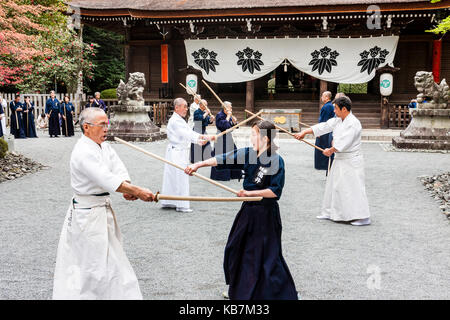 Japan, Osaka, Tada. Master samurai swordsman dressed in white fighting with woman in black, using bokken, or bokuto, wooden swords in shrine grounds. Stock Photo