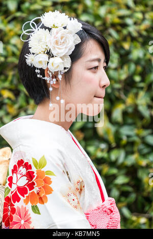 Japan. Head and shoulders side view of young Japanese woman in cream coloured kimono. White flowers in hair. Pensive expression. Stock Photo