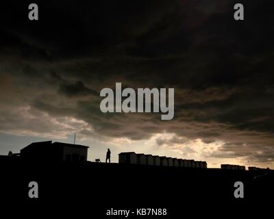 AJAXNETPHOTO. 2017. WORTHING, ENGLAND. - RAIN CLOUDS - MOISTURE LADEN CUMULO STRATUS CLOUDS DRIFT OVER BEACH HUTS AND A DOG WALKER ON THE SEAFRONT. PHOTO:JONATHAN EASTLAND/AJAX REF:GR4172009 7190 Stock Photo