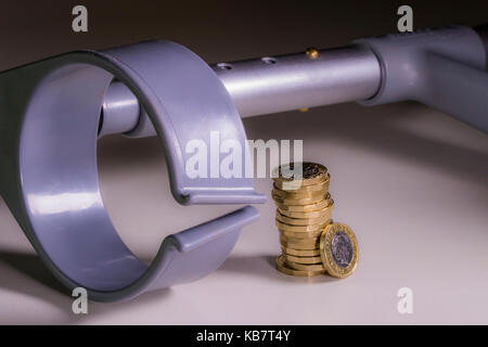 A crutch and new sterling pound coins. Concept of link between incapacity and UK pounds sterling, such as disability income and healthcare cost. Stock Photo