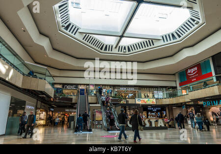 Inside Queensgate Shopping Centre, with people and an escalator to the ground floor and first floor. Peterborough city, Cambridgeshire, England, UK. Stock Photo