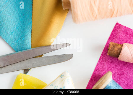 sewing, patchwork, tailoring and fashion concept - closeup tools on white work desk in studio, scissors, spools of blue and pink threads, pincushion,  Stock Photo