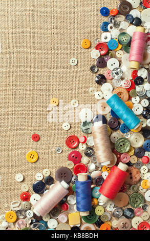 Colourful sewing buttons and spools of threads on fabric texture background with copy space Stock Photo