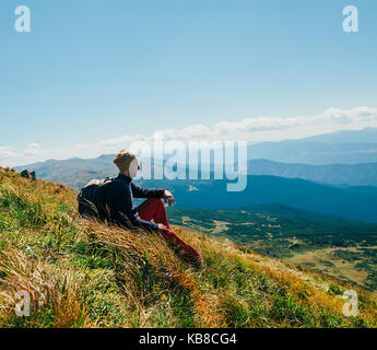 Handsome young man sitting on rocky cliff and enjoying nature. back view Stock Photo