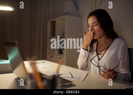 tired woman with papers yawning at night office Stock Photo